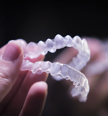 Woman hand holding invisible orthodontics. Black background.
