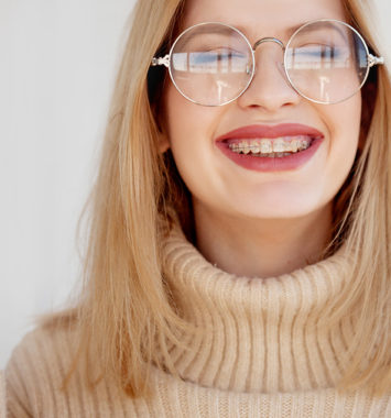 Stylish and beautiful young blonde with glasses and beige oversize sweater. Young woman wearing braces and smiling